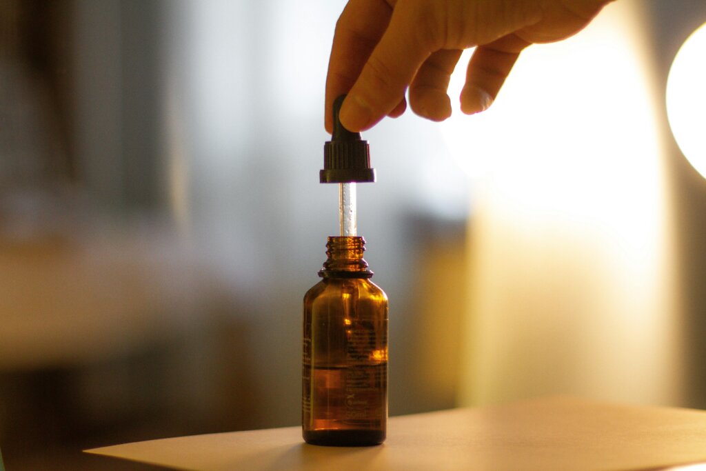 A hand holding a serum dropper over a brown glass bottle with a blurred background.