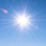 A stunning winter mountain landscape with a bright sun and clear blue sky.