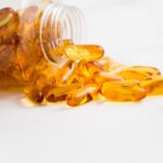 Close-up of fish oil capsules spilling from a bottle on white background.