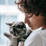 A woman with curly hair gently cradles her gray cat, creating a serene indoor moment.