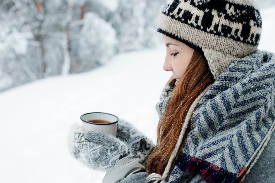 Woman in winter attire holding a hot beverage outdoors in snowy surroundings.