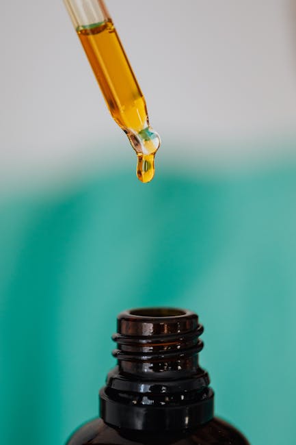 A dropper carefully adding liquid into a brown glass bottle with a turquoise background.